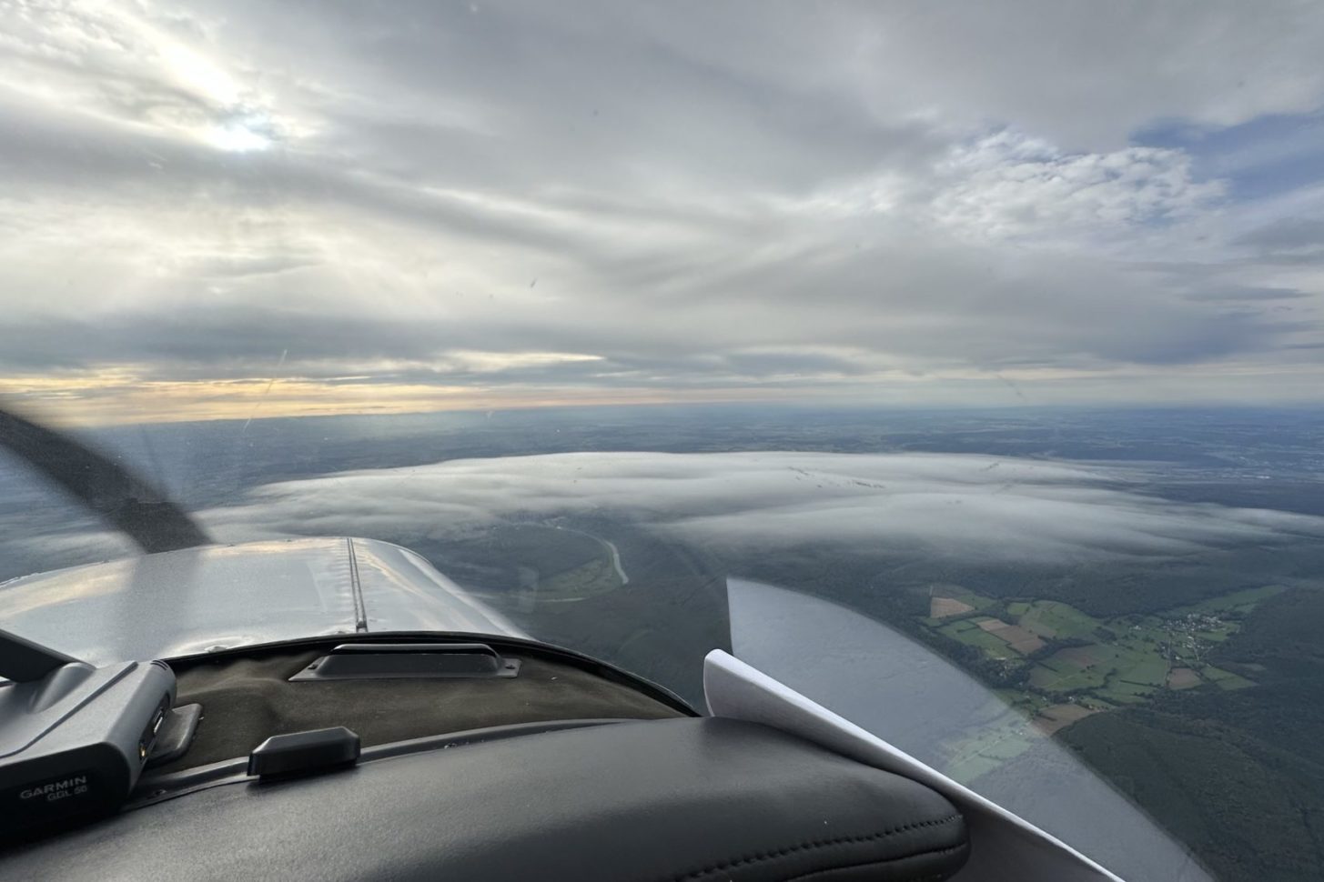 Blick aus dem Cockpit im Flug mit einer geschlossene Wolkendecke über und Wolkenfetzen unter dem Flugzeug.