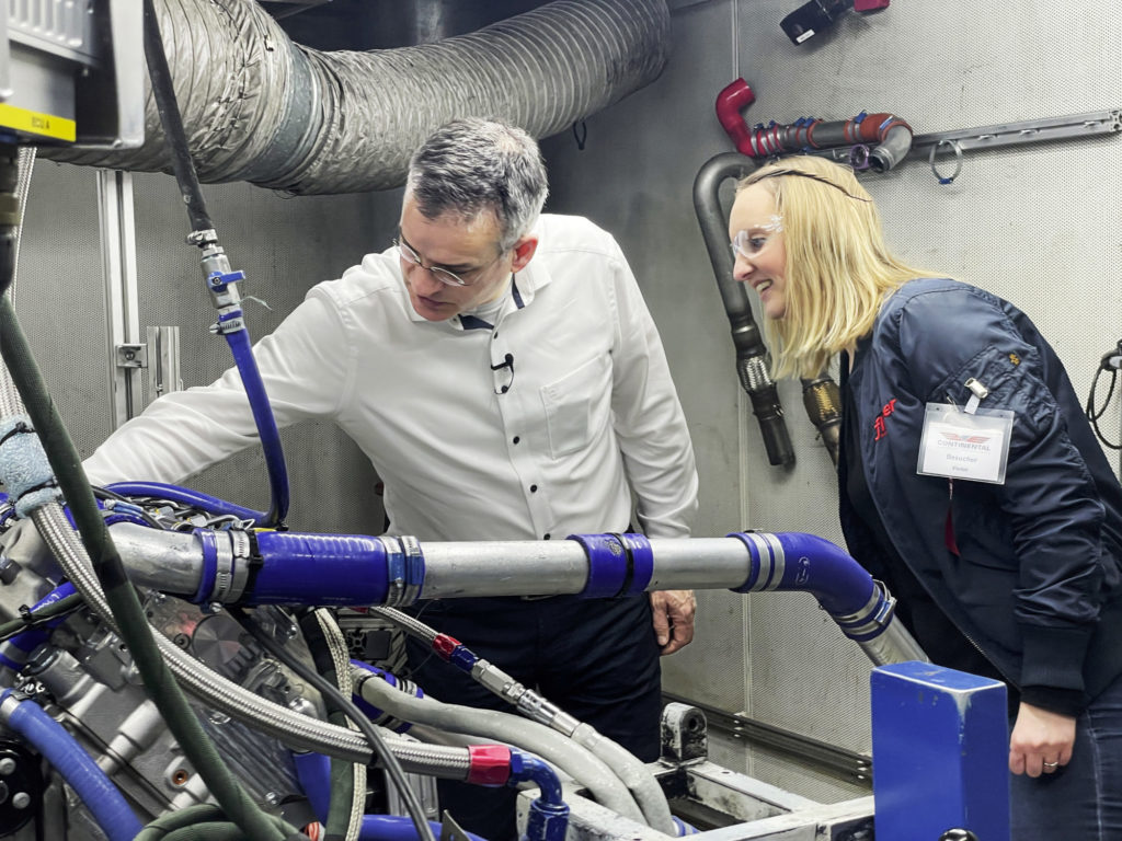 Isabella Sauer steht mit dem Trainingschef von Continental Aerospace Technologies an einem Prüfstand für Dieselmotoren.