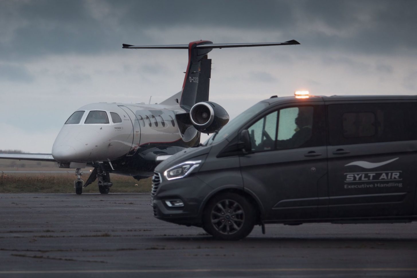 Ein Embraer Phenom 300 steht hinter einem Bodenfahrzeug der Sylt Air.